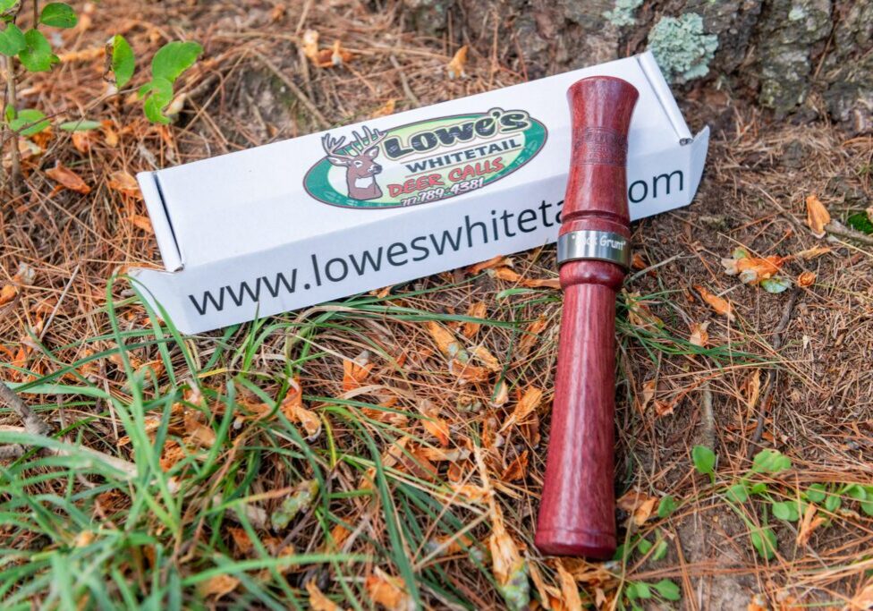 A red pipe laying in the grass next to a box of matches.